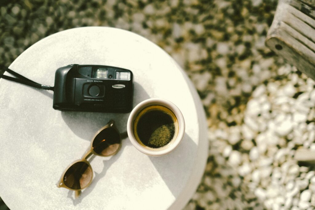 Flat lay of coffee cup, sunglasses, and camera on a sunny summer day outdoors.